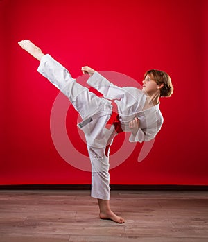 Young girl karateka in a white kimono and a red belt trains and performs a set of exercises on a bright red background