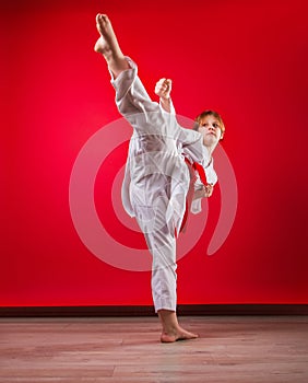 Young girl karateka in a white kimono and a red belt trains and performs a set of exercises on a bright red background