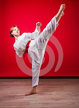 Young girl karateka in a white kimono and a red belt trains and performs a set of exercises on a bright red background