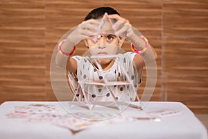 Young girl kid busy in building Pyramid with house of cards at home - concept of focus or concentration excerise game