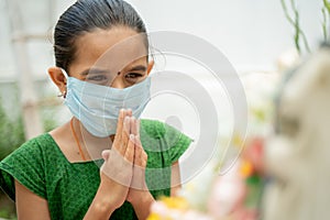 Young girl kid in medical mask praying to god to protect from coronavirus or covid-19 by folding hands in namaste