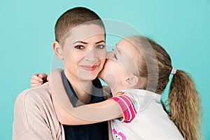 Young girl kissing mother, young cancer patient, on the cheek. Cancer and family support.