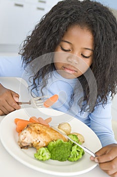 Young girl in kitchen eating chicken and vegetable