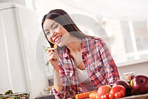 Young girl at kitchen healthy lifestyle leaning on table eating carrot looking camera laughing cheerful