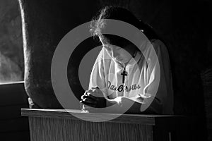 Young girl kneeling in prayer pose, head lowered, eyes closed with clasped hands. Pray in silence, believe in God concept