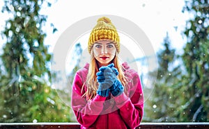 Young girl in a knitted cap and mittens standing under snowing