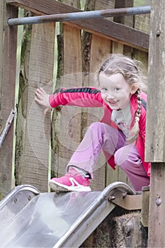 Young girl laughing and smiling at top of slide at outdoor adventure playground