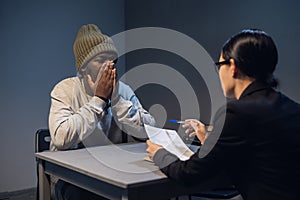 A young girl lawyer consults her client at the police station, a black guy in a cap and handcuffs.