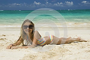 Young girl laying down on white sandy beach.