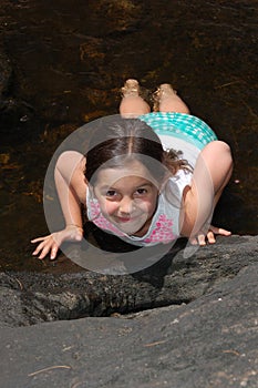 A young girl laying on her stomach in a country brook