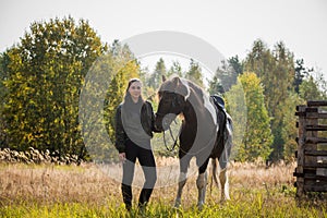 A young girl leads her horse by the bridle along a path along the fence