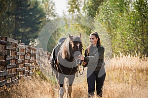 A young girl leads her horse by the bridle along a path along the fence