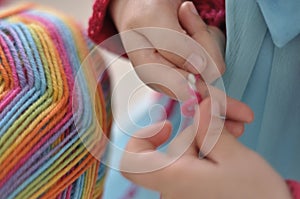 Young girl learning to crochet with multicoloured wool yarn. Homemade handiwork can be a nice and creative present