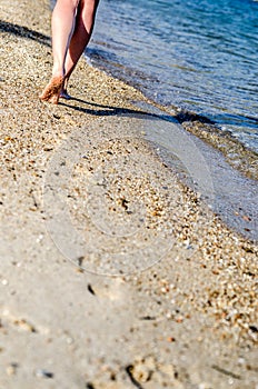 A young girl leaves traces on the sand, walking along the coast.