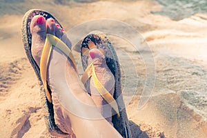 Young girl legs and flip-flop on the sand beach
