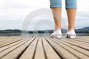 Young girl legs with white shoes and blue jeans on a wooden pier