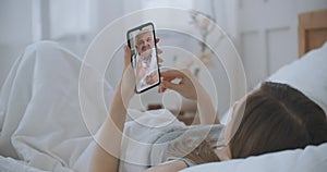 Young Girl lie in bed at Home Using Smartphone to Talk to Her Doctor via Video Conference Medical App. Beautiful Woman