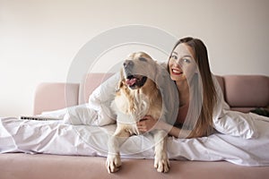 young girl lies on a bed with a golden retriever dog and smiles, a woman with pet rest at home