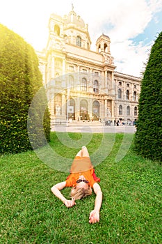 A young girl lies on the grass and rests against the backdrop of the Natural History Museum in Vienna, Austria