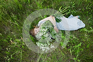 Young girl lies on green grass hugs white flowers in blue dress