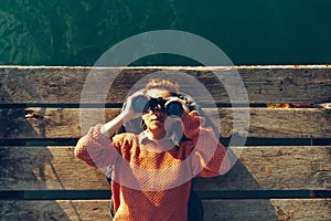 Young Girl Lies On A Pier Near The Sea And Looks Through Binoculars. Travel Search Journey Concept