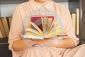 Young girl in a light dress is reading a book. Female hands hold a book in their hands