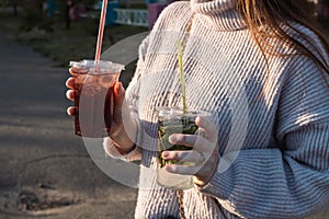 A young girl in a light sweater holds two cocktails in her hands in the rays of sunset