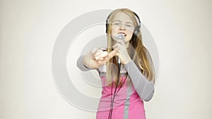 Young girl listening music on headphones holding microphone, singing and funny dancing