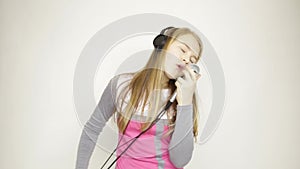 Young girl listening music on headphones holding microphone, singing and funy dancing