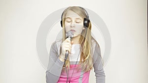 Young girl listening music on headphones holding microphone, singing and funy dancing