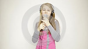 Young girl listening music on headphones holding microphone, singing and funy dancing