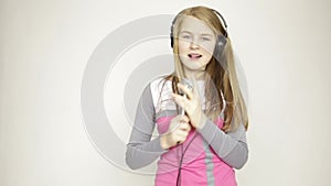 Young girl listening music on headphones holding microphone, singing and funy dancing