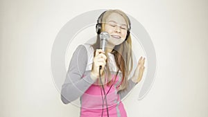 Young girl listening music on headphones holding microphone, singing and funy dancing