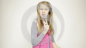 Young girl listening music on headphones holding microphone, singing and funy dancing