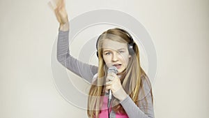 Young girl listening music on headphones holding microphone, singing and funy dancing