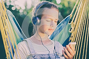 Young girl listening to music with headphones lying in a hammock on a sunny day