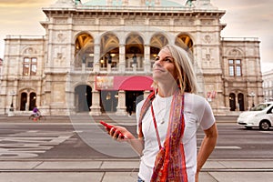 Young girl listens to music with headphones in front of Vienna State Opera, Austria