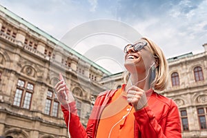 Young girl listens to music with headphones in front of Vienna State Opera, Austria