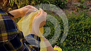 A young girl with long blond hair knits a yellow sweater in the garden in the summer. woman makes clothes with hands closeup