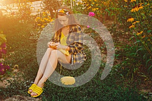 A young girl with long blond hair knits a yellow sweater in the garden in the summer. woman makes clothes with hands closeup