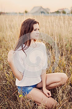 Young girl with long brown hair sitting in autumn field, smiling