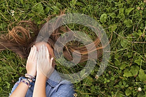 Young girl with long hair, closing eyes while lying in the green grass. Relax.