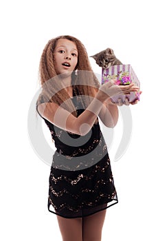 Young girl with long hair in a festive black dress with a gray kitten in a gift box in his hands