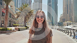 A young girl with long hair and a good mood walks along the embankment of Dubai Marina.