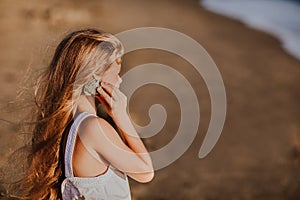 Young girl with long hair holding and listening the seashell. Focus is at the shell. Copy space