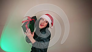 A young girl with long hair in a red hat of Santa's assistant with a gift in her hands. Christmas advertisement