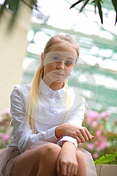 Young girl with long white hair in a white formal shirt and a short light skirt walks in the garden