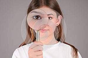 Young girl with look through magnifying glass over gray background. Teengirl showing her eye. Vision diagnostics