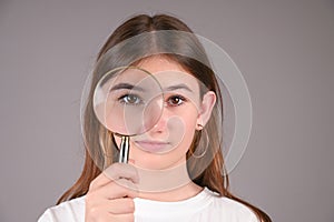 Young girl with look through magnifying glass over gray background. Teengirl showing her eye. Vision diagnostics