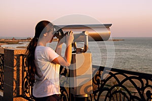 Young girl looking through a coin operated binoculars on the sea shore of Cannes, France.